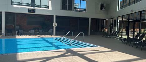 Una piscina interior con agua cristalina y azul, rodeada de sillas de descanso y un techo iluminado por tragaluces.