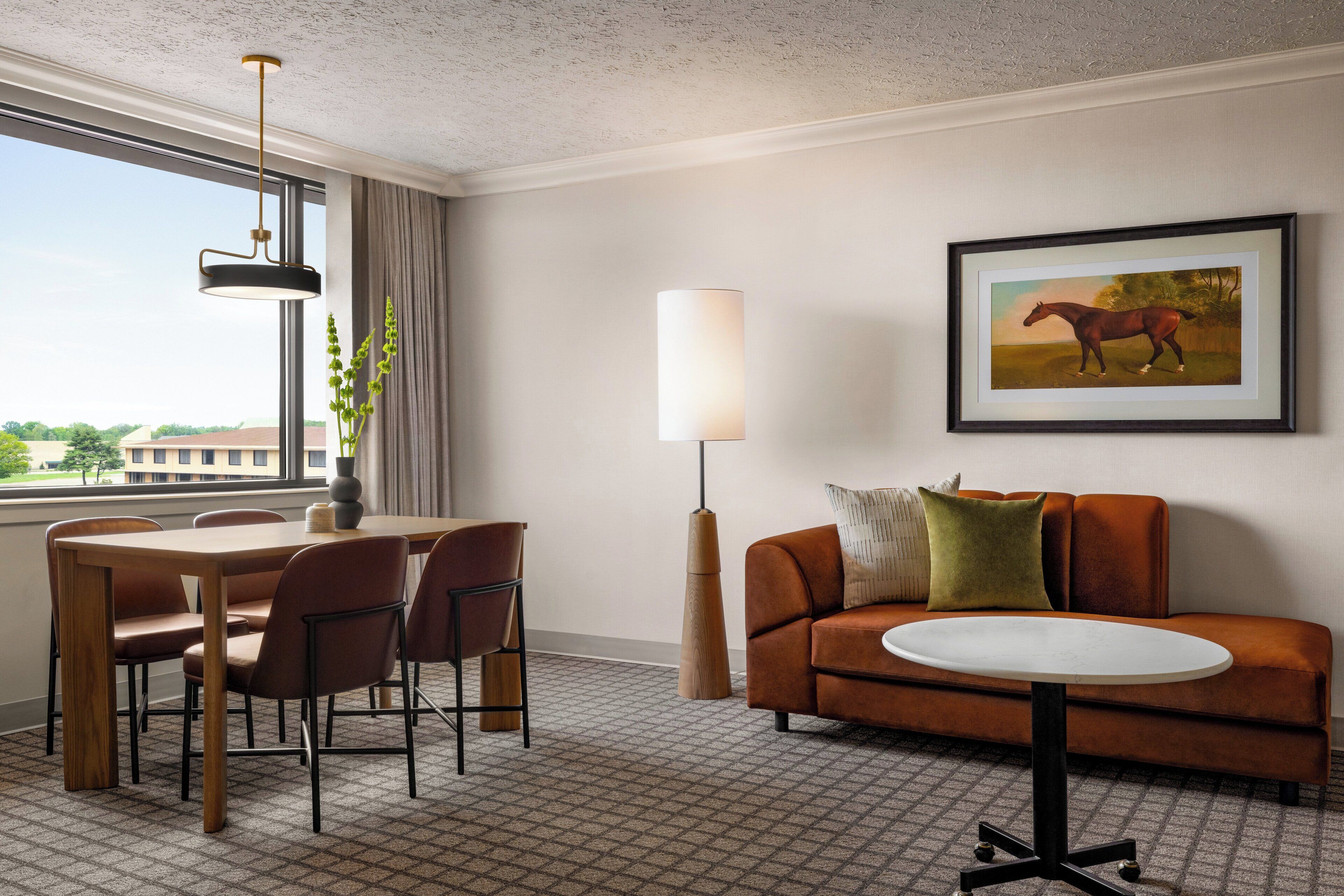 A hotel room with a dining table, chairs, a sofa, a lamp, and a framed picture on the wall.