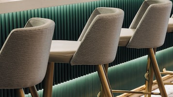 A row of bar stools with a woven seat design and gold legs, positioned in front of a green upholstered bench.