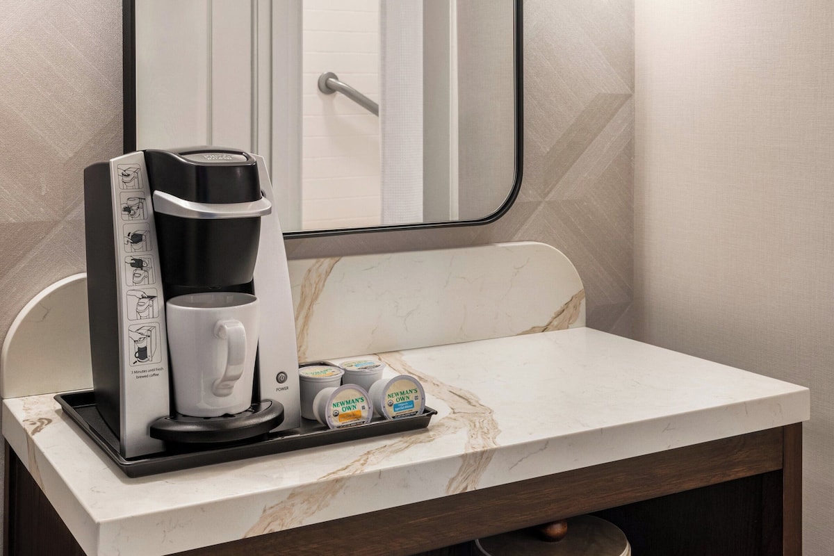 Une salle de bain moderne avec un grand miroir, une machine à café et un plateau de produits de toilette.
