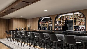 A bar area with a long counter, multiple stools, and shelves stocked with bottles. - Crowne Plaza Louisville Airport Expo Ctr by IHG (Louisville)