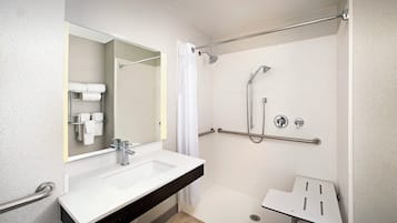 Une salle de bain moderne avec un lavabo blanc, un miroir, une douche équipée d’un pommeau de douche à main et d’une barre d’appui.