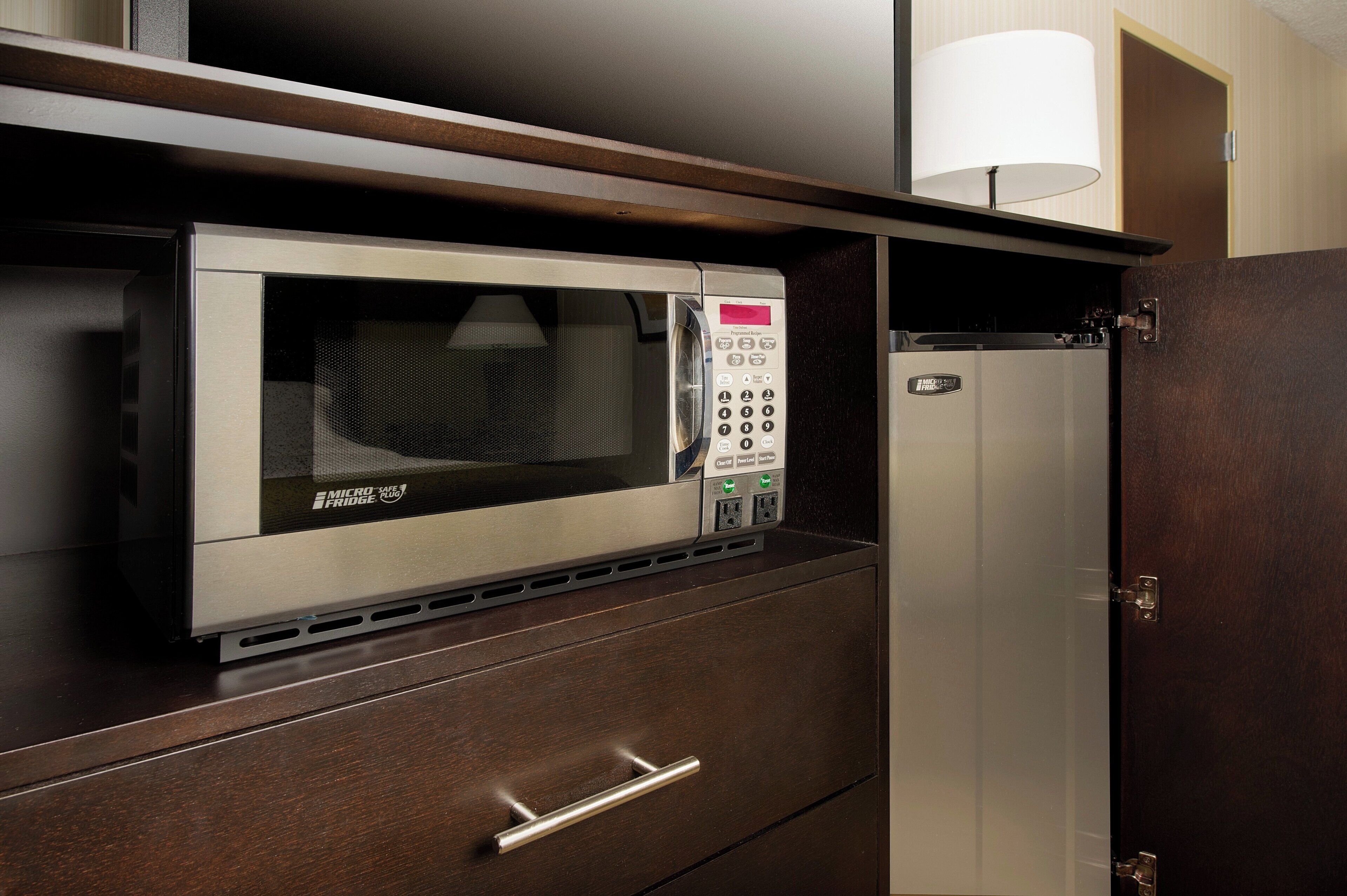 A microwave oven with a digital display and control panel, mounted on a wooden cabinet with a drawer below.