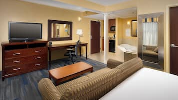 A hotel room with a bed, a desk, a television, a chair, a sofa, and a bathroom visible through an open door.
