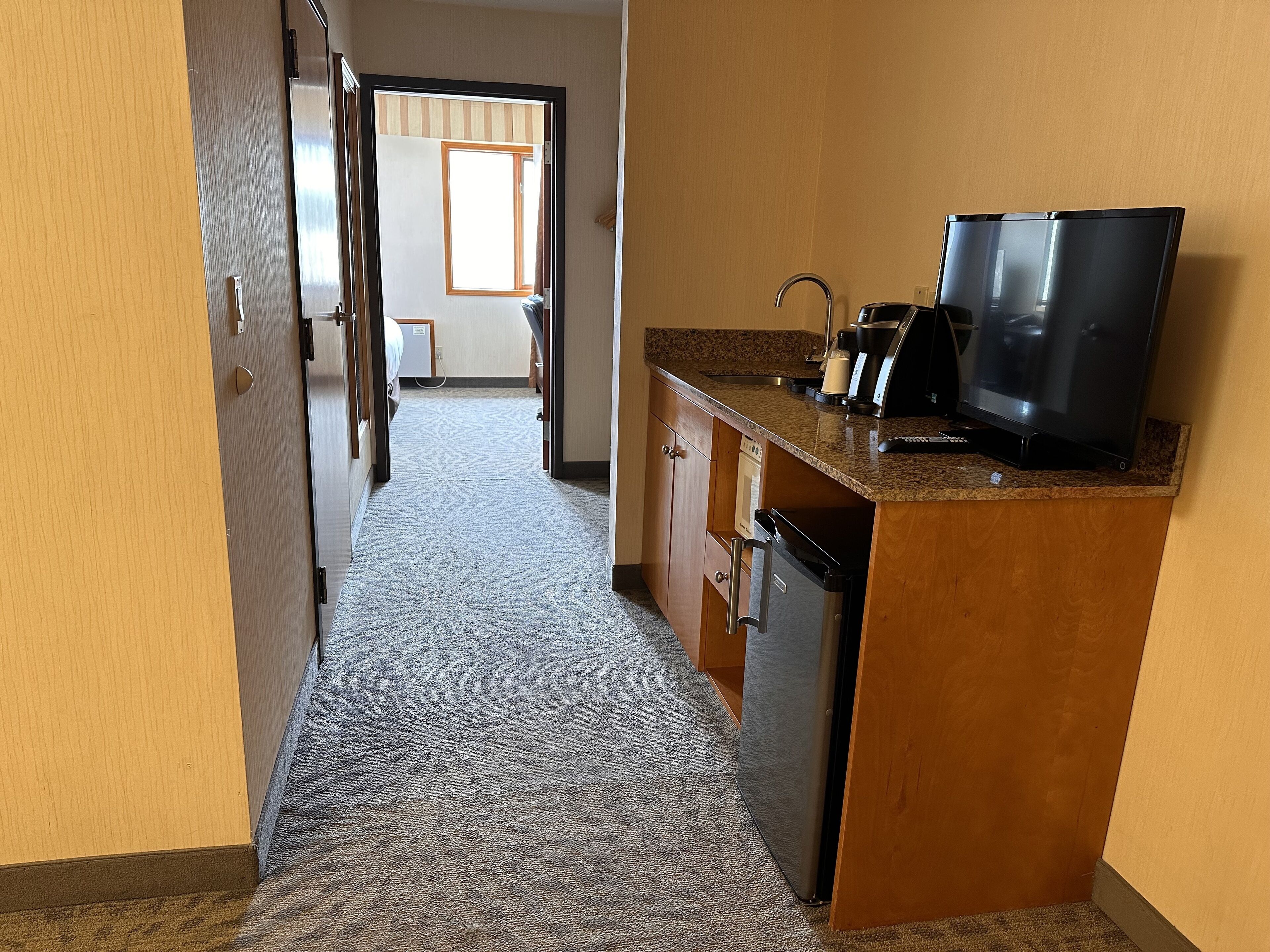 A hotel corridor with a kitchenette area featuring a microwave, coffee maker, and a television.