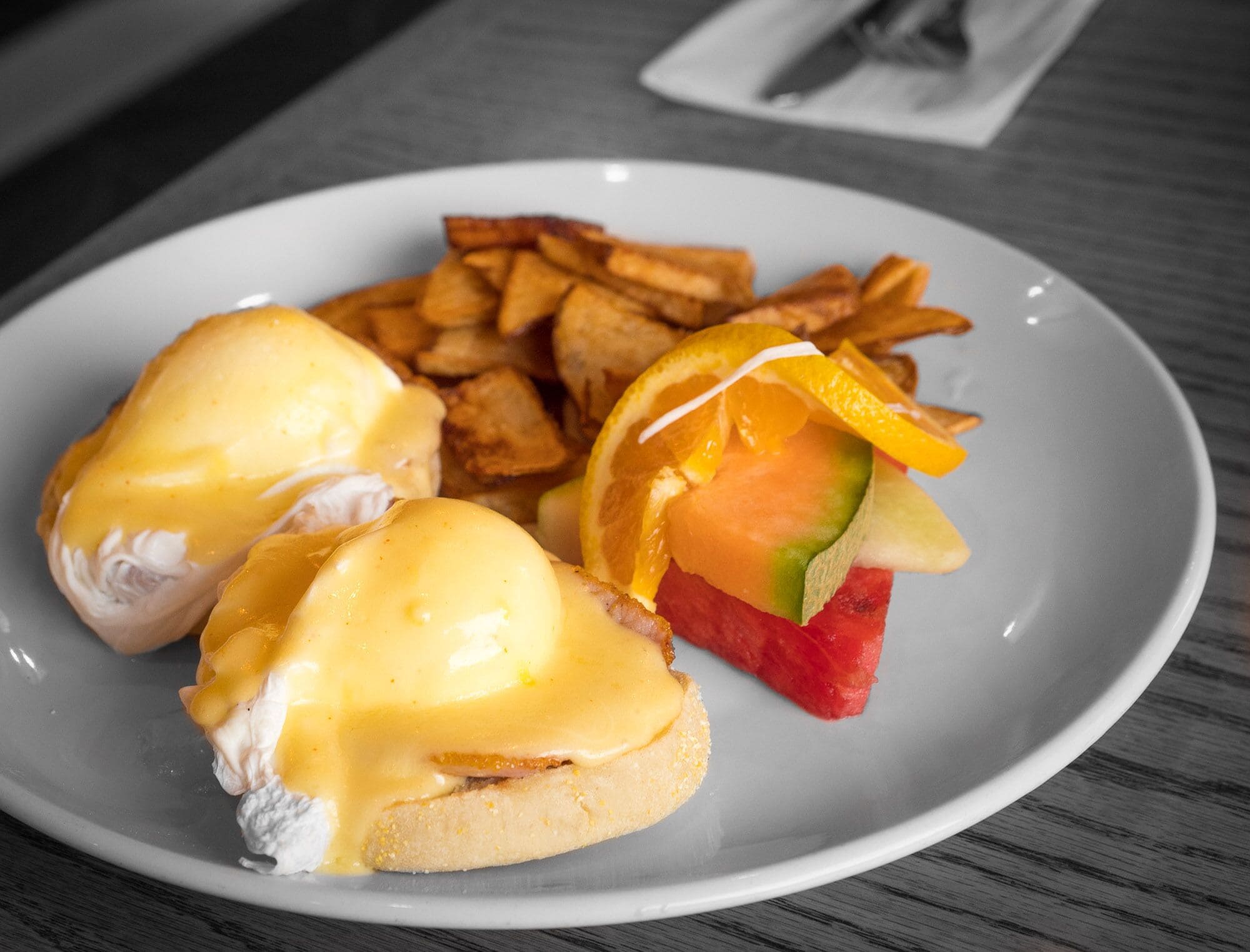 Un plato con huevos benedictinos, patatas ralladas y una rebanada de sandía.