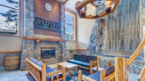 Un interior acogedor con chimenea de piedra, muebles de madera y un amplio ventanal con vistas a montañas nevadas.
