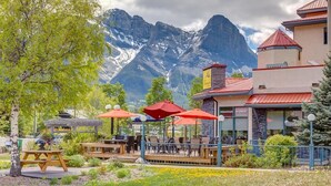 Un restaurante con terraza al aire libre, un paisaje montañoso de fondo y un edificio de piedra con techo rojo.