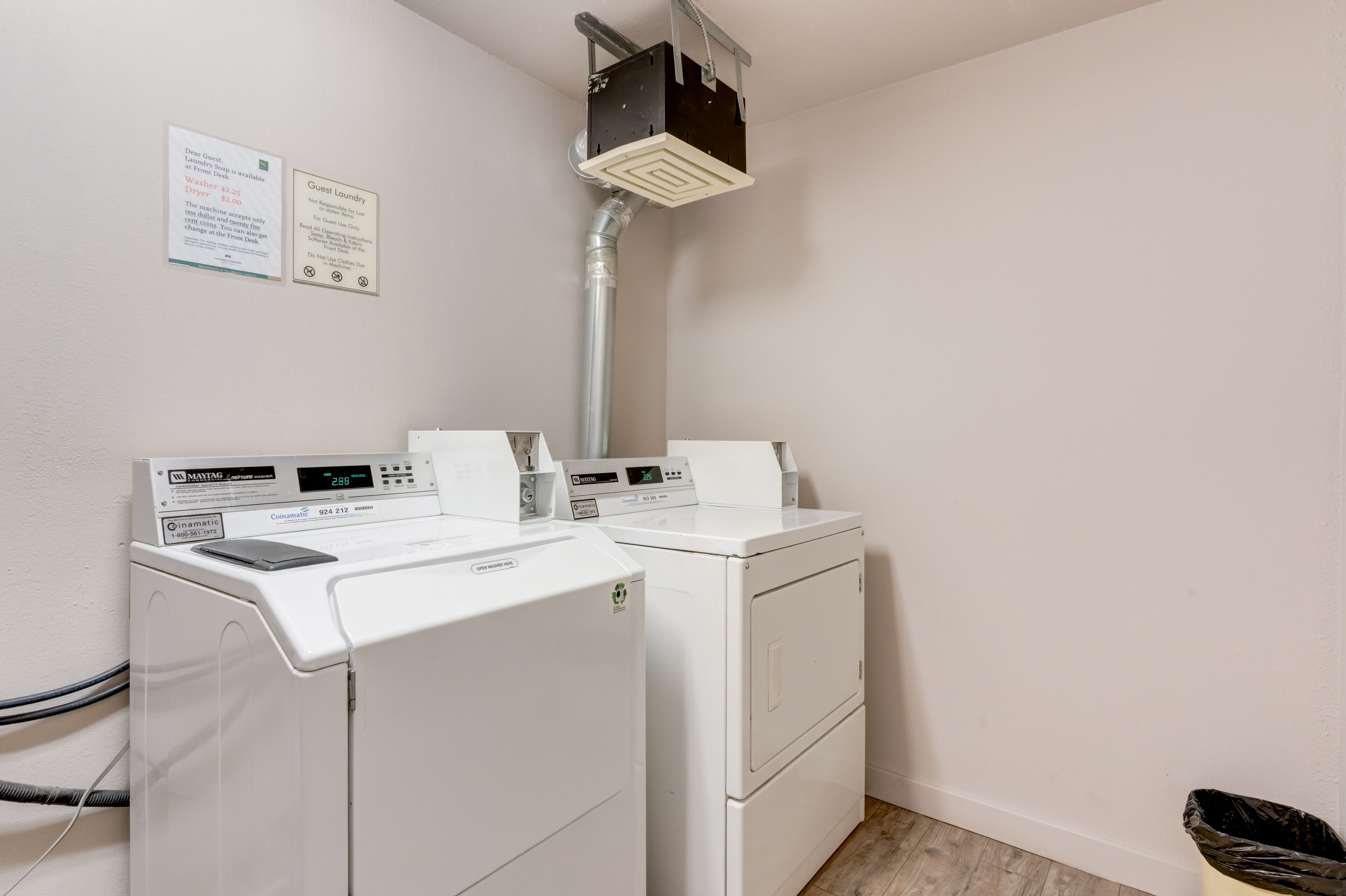 A laundry area with two front-loading washing machines, a dryer, and a vent system.