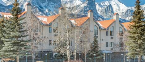A hotel with a snow-covered mountain backdrop, featuring a traditional architectural style with multiple chimneys and a red roof.