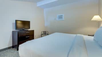Habitación de hotel con una cama, un televisor sobre una cómoda, una lámpara y un equipo de aire acondicionado instalado en la pared.