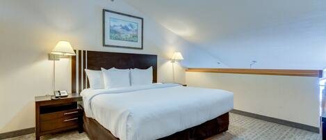 A hotel room with a large bed, two bedside tables with lamps, a framed picture on the wall, and a carpeted floor.