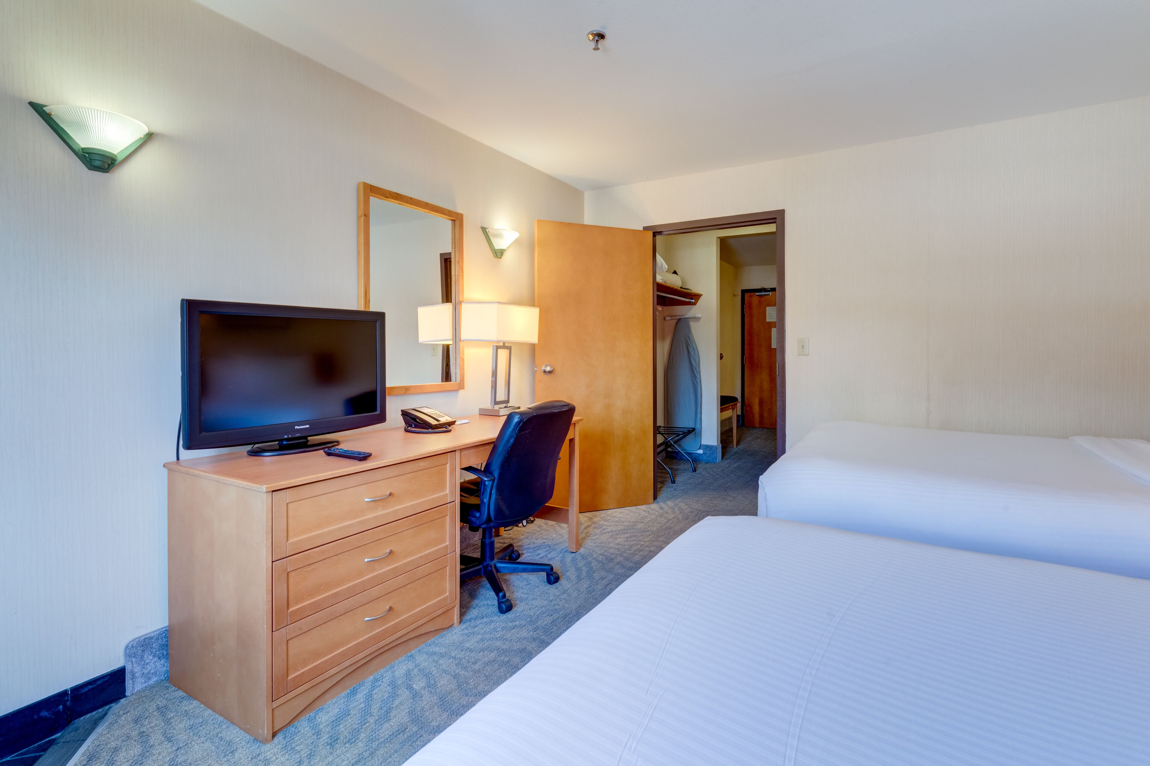 Una habitación de hotel con cama, escritorio, computadora, televisor y armario.