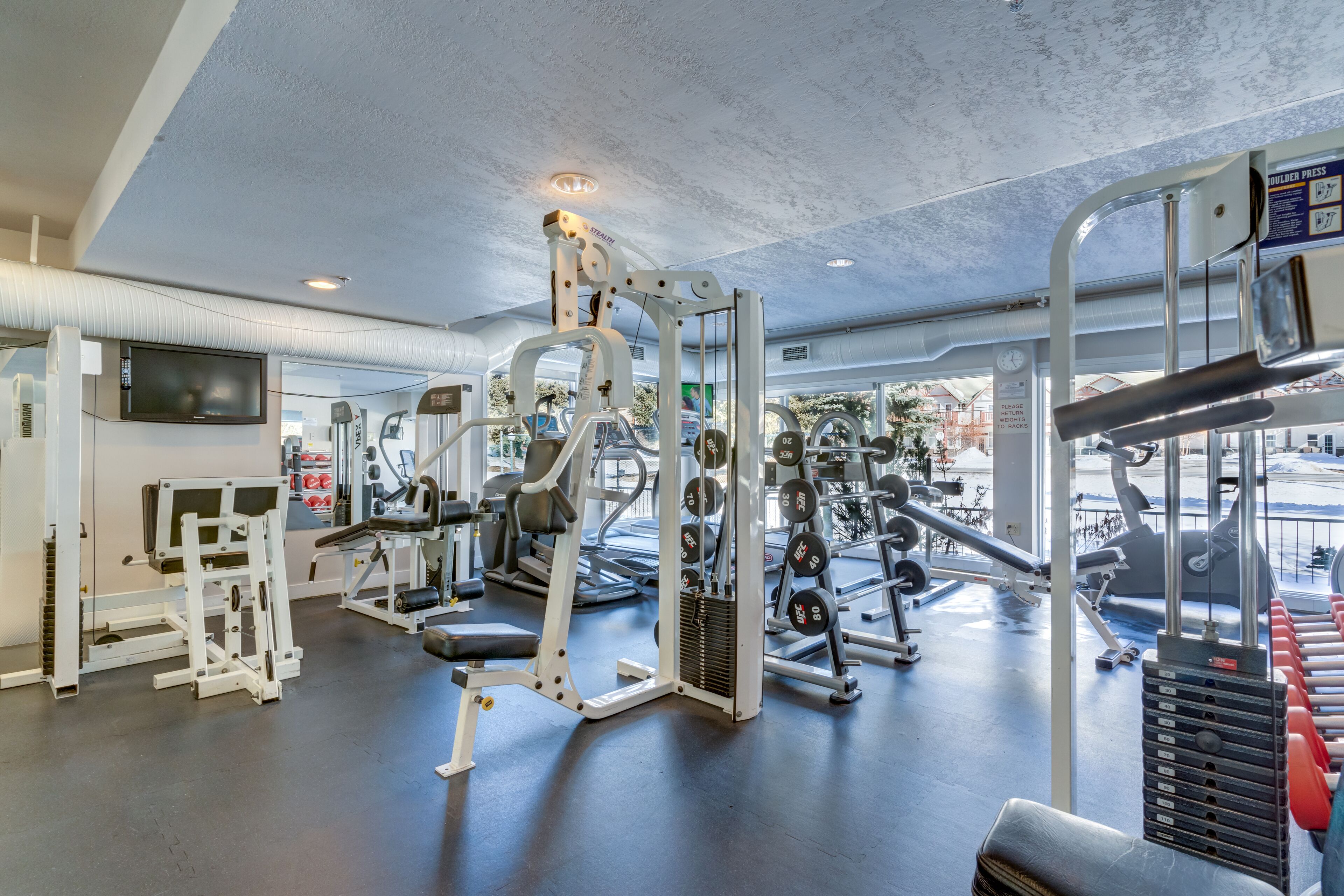 A gym with various exercise machines, a television, and a view of the outside.