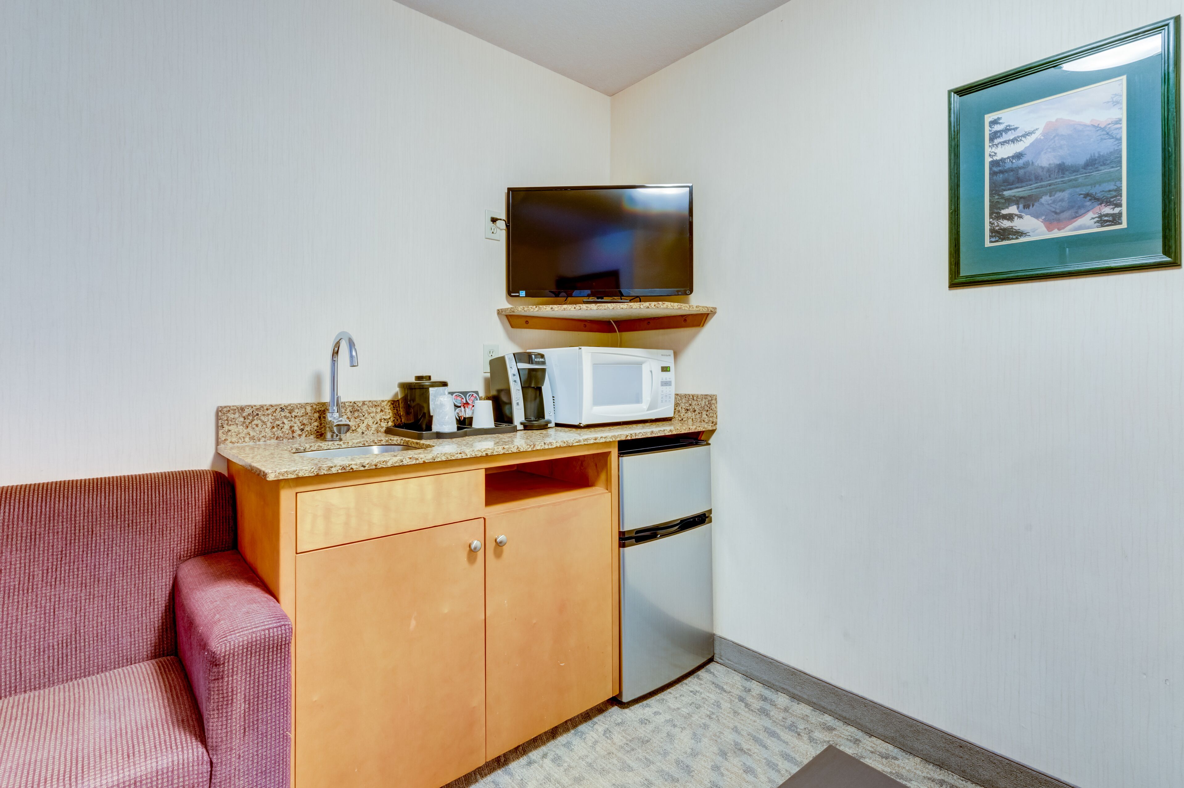 A compact kitchenette with a microwave, toaster, and sink. A flat-screen TV is mounted above the counter.