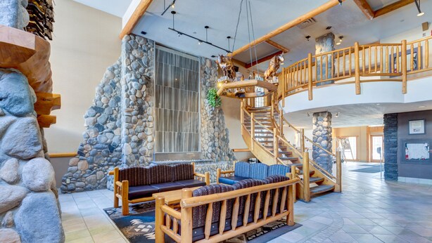 Un vestíbulo amplio con pared de piedra, bancos de madera, una escalera y un ventanal grande.