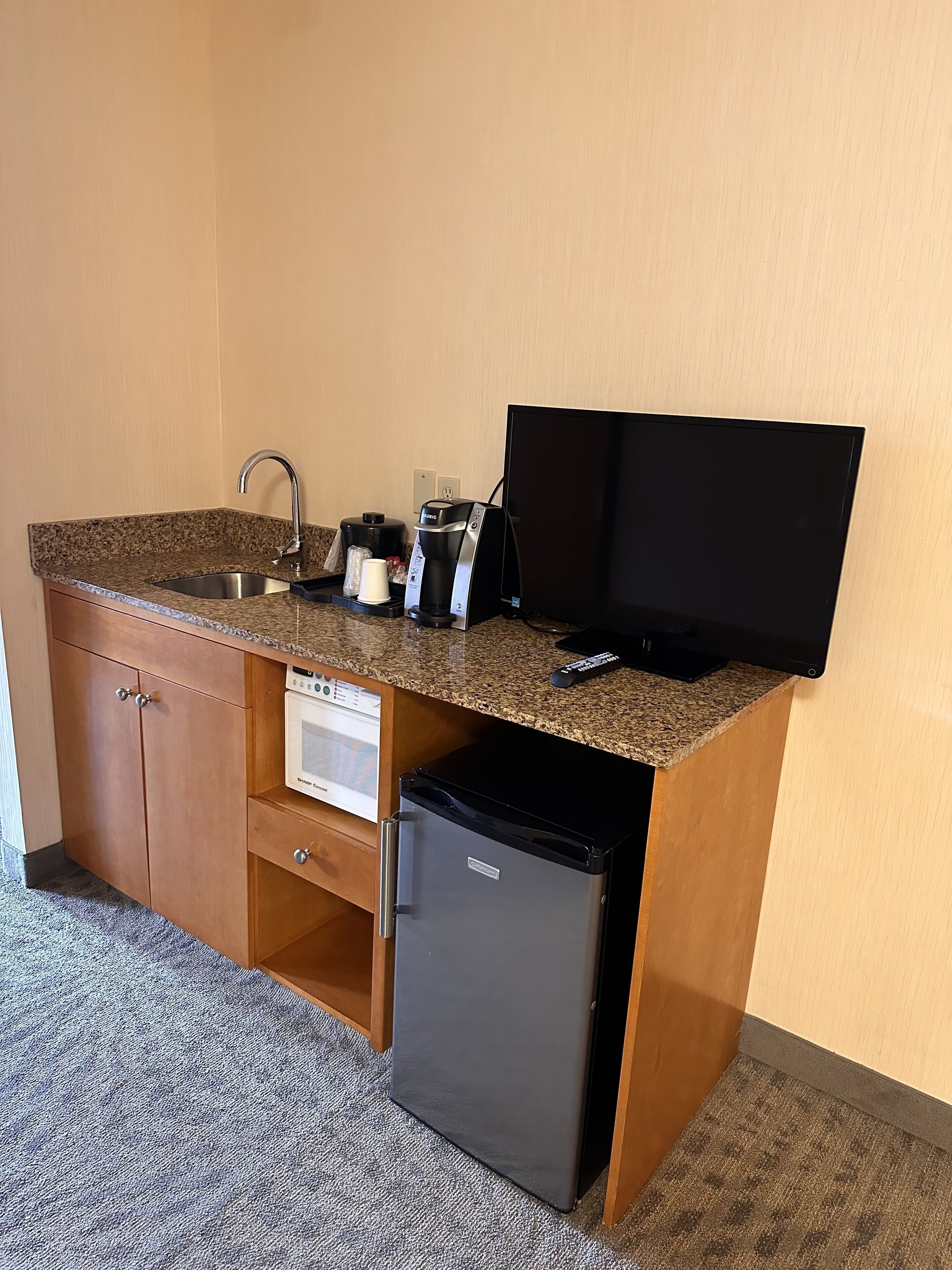A compact kitchenette with a built-in refrigerator, a coffee maker, a microwave, and a flat-screen TV.
