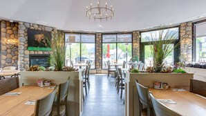 Un restaurante con paredes de piedra, mesas y sillas de madera. Se observa un candelabro colgando del techo.