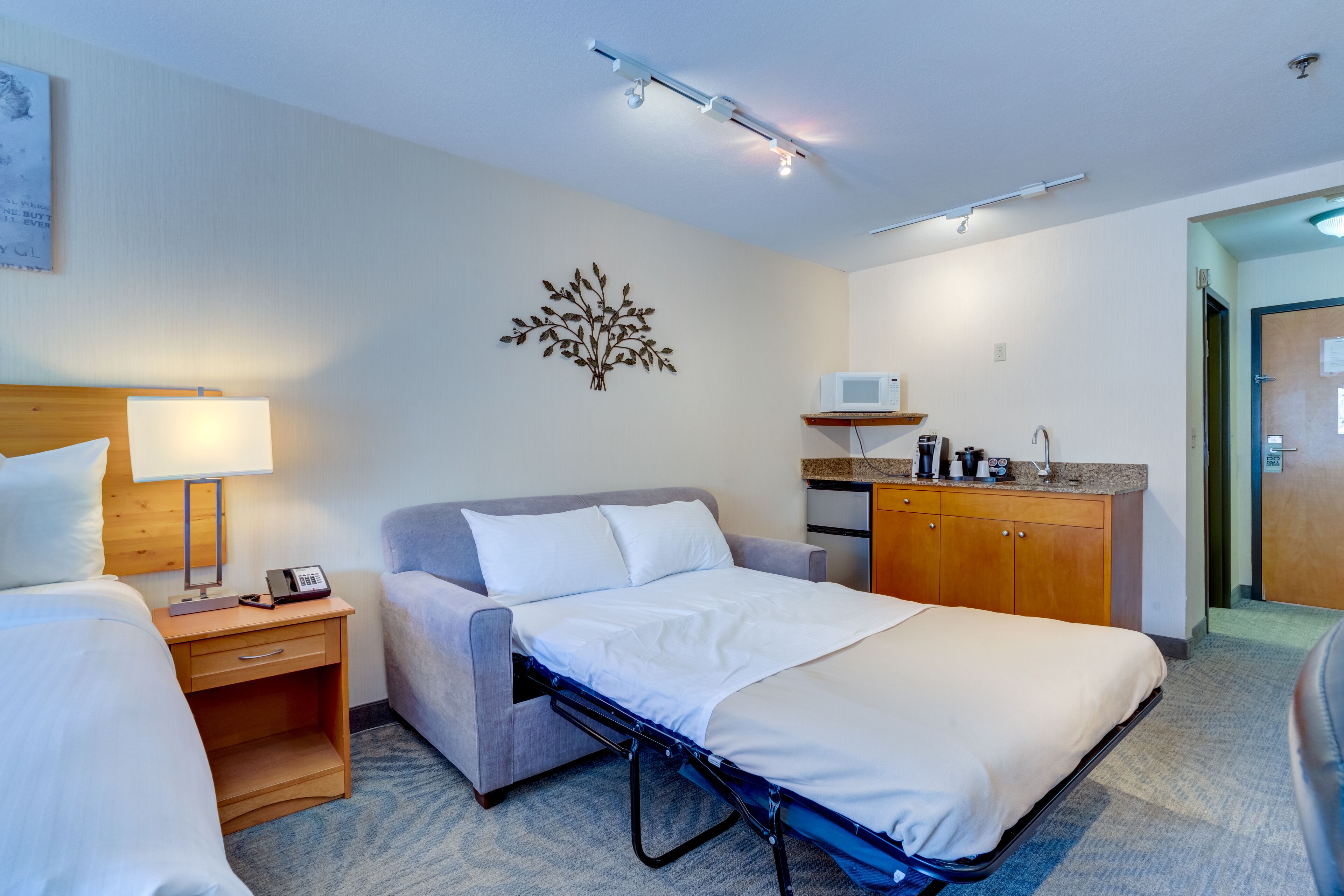 Une chambre d’hôtel comprenant un lit, une table de chevet avec une lampe, un petit bureau, un four à micro-ondes et un placard.