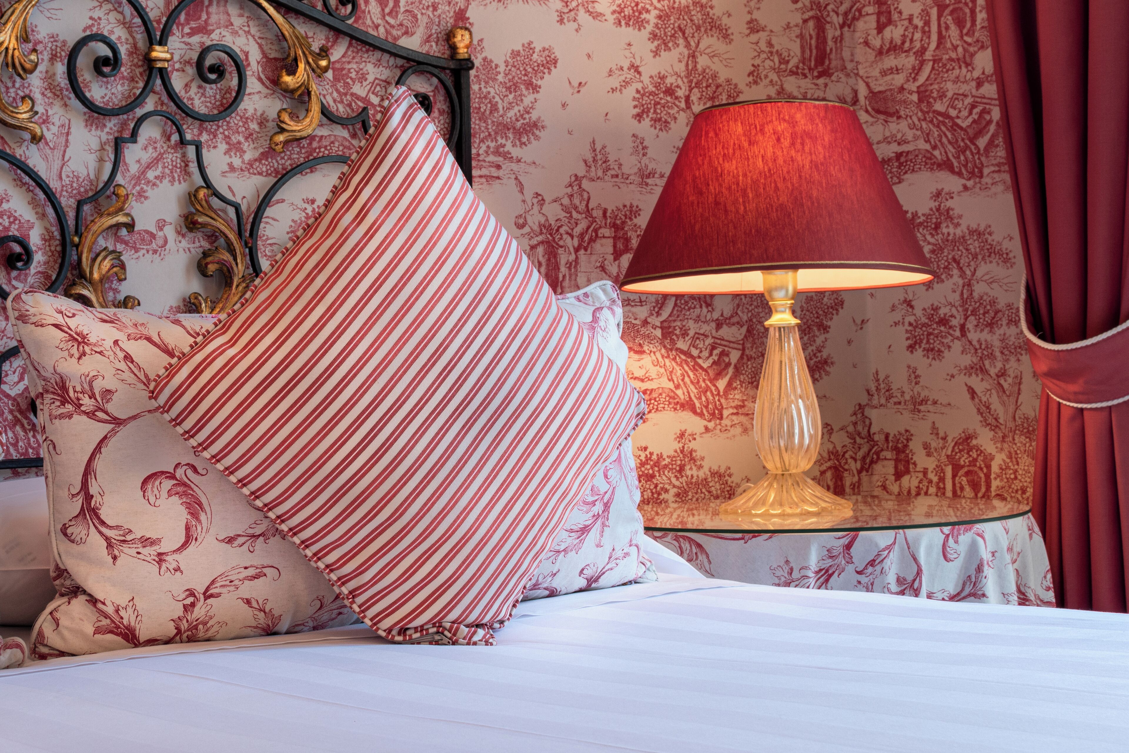 A bed with striped pillows, a red lamp, and a patterned wall.