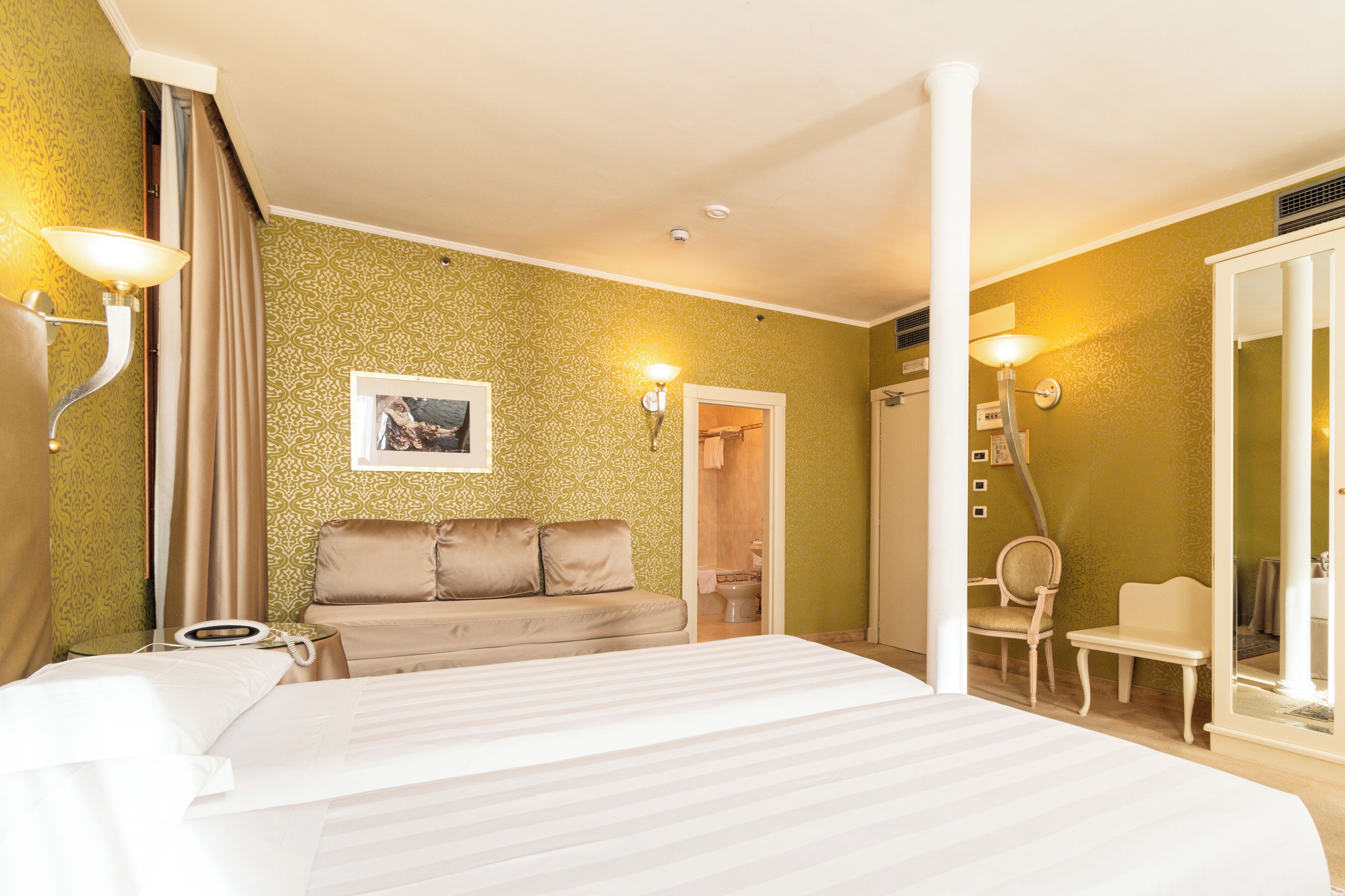 A hotel room with a large bed, a sofa, a chair, and a wardrobe.