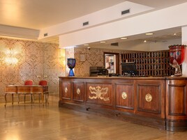 Un'area di accoglienza con una scrivania in legno, sedie, un vaso, una libreria con chiavi e una scultura decorativa a forma di mano.