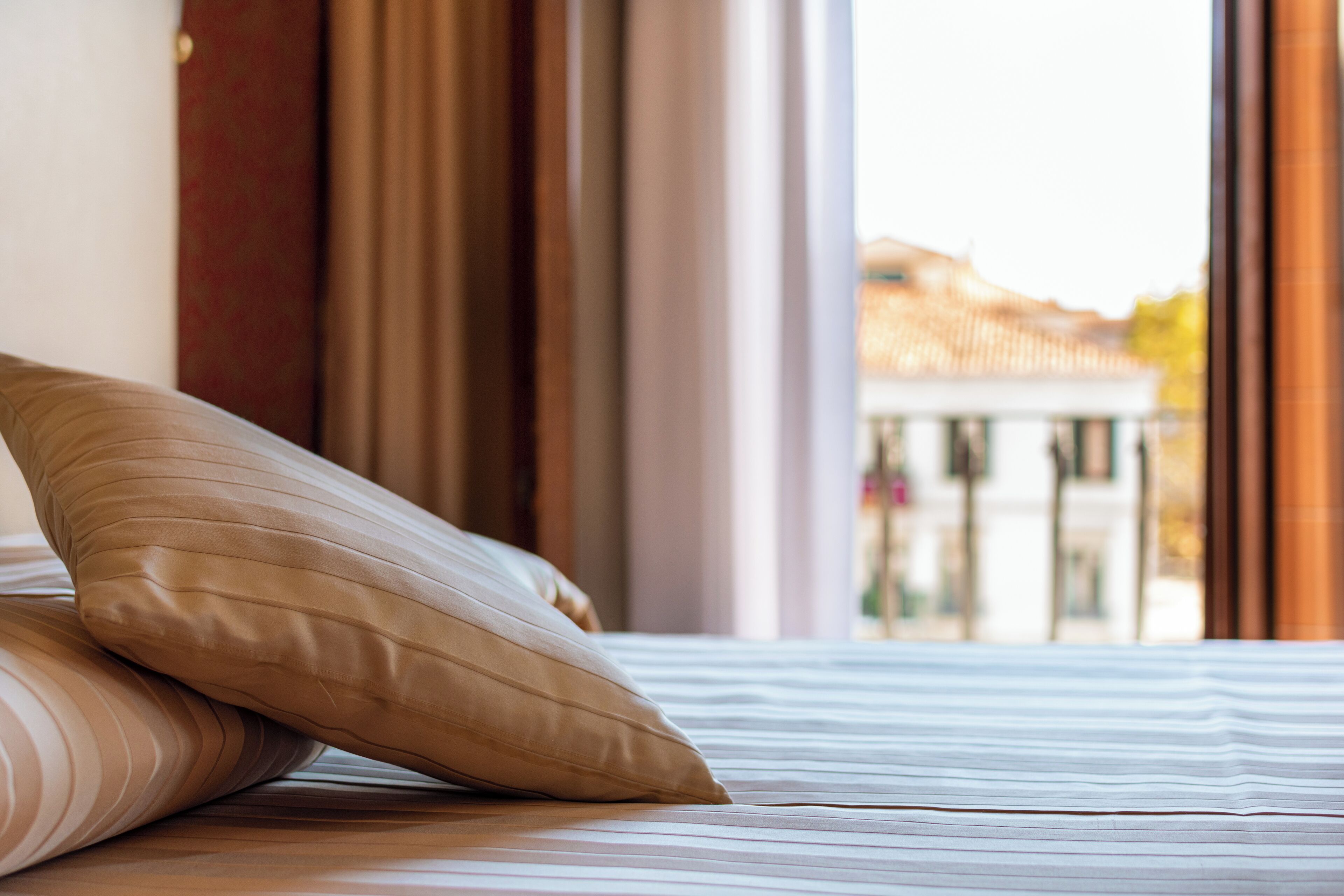 A bed with striped bedding and a pillow, a window with curtains, and a view of a building outside.