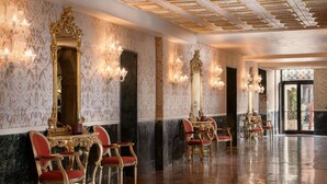Un salón amplio con candelabros ornamentados, espejos con marcos dorados y sillones tapizados en rojo.