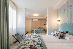 Una habitación de hotel con cama, sofá, una mesita y ventana con cortinas.