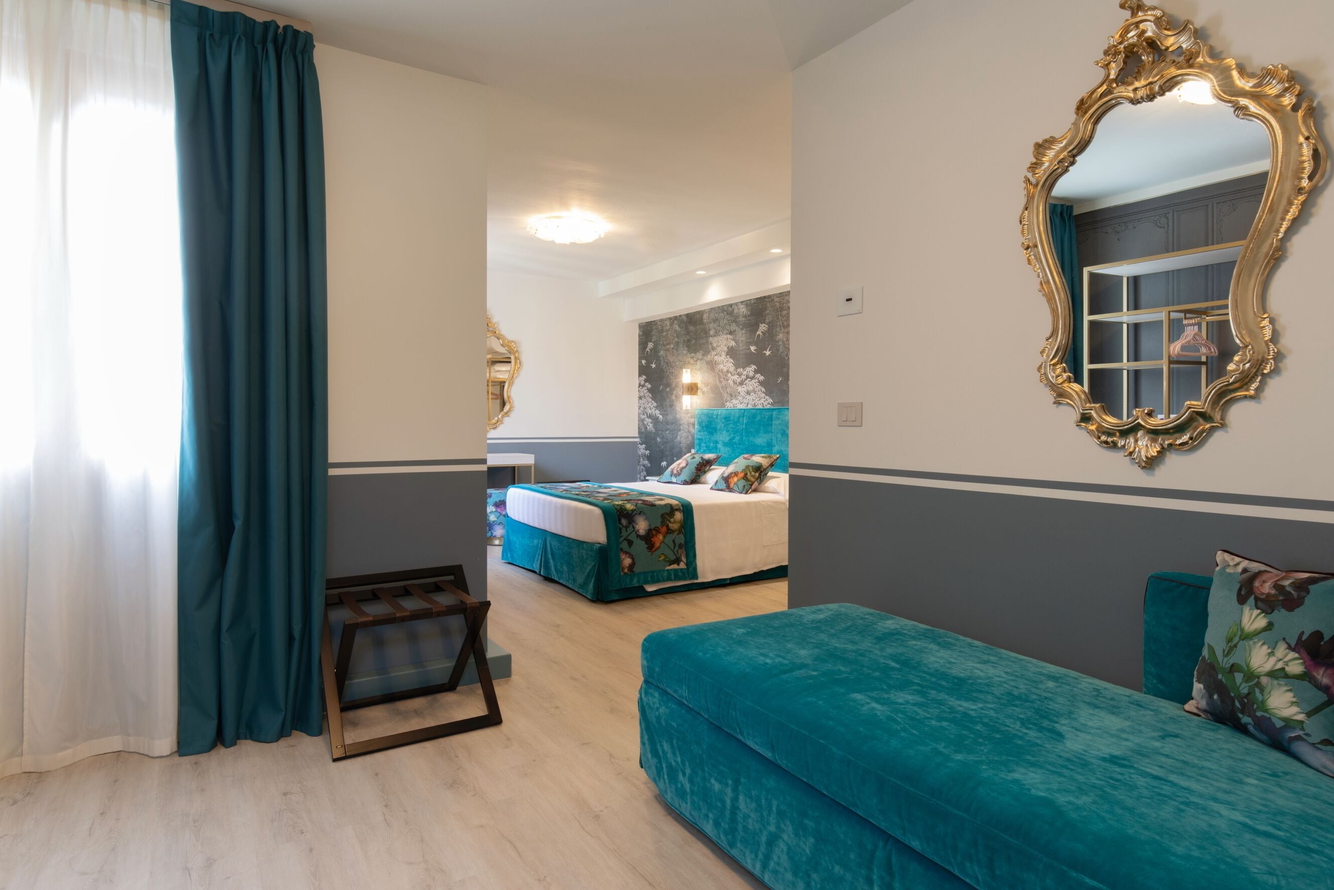 A hotel room with a bed, a sofa, a mirror, and a window with curtains.