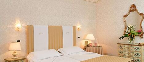 A hotel room with a bed, two bedside tables, a dresser, a mirror, and wall sconces.