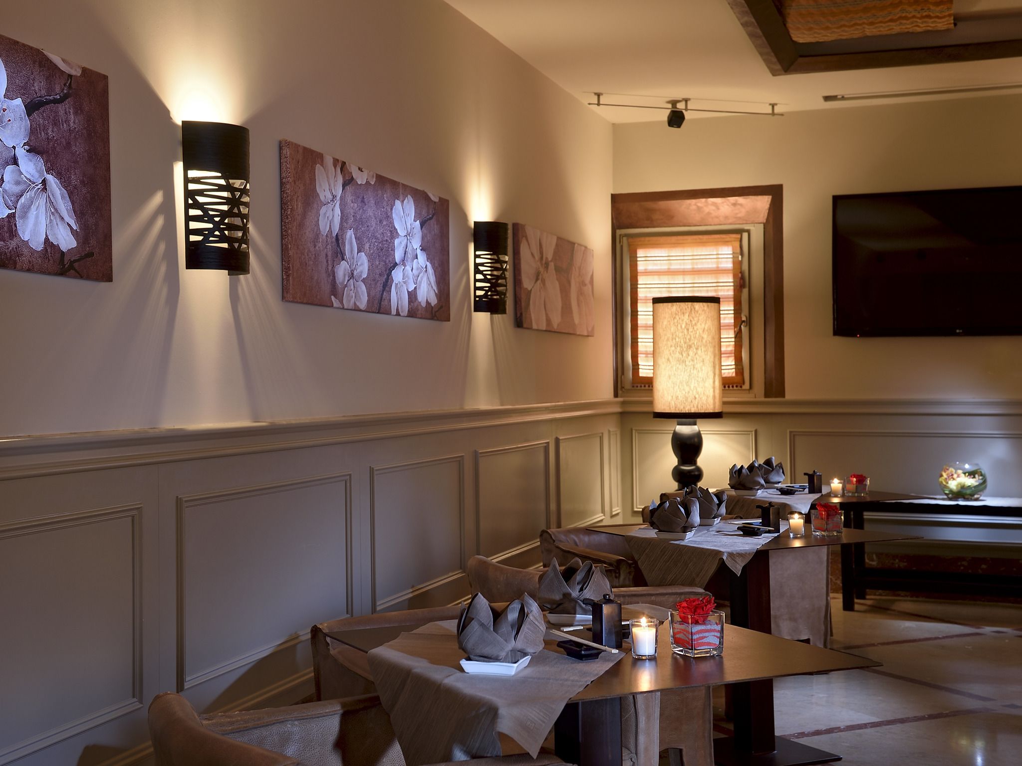 A dining area with a long table, multiple chairs, wall-mounted artwork, and a television.