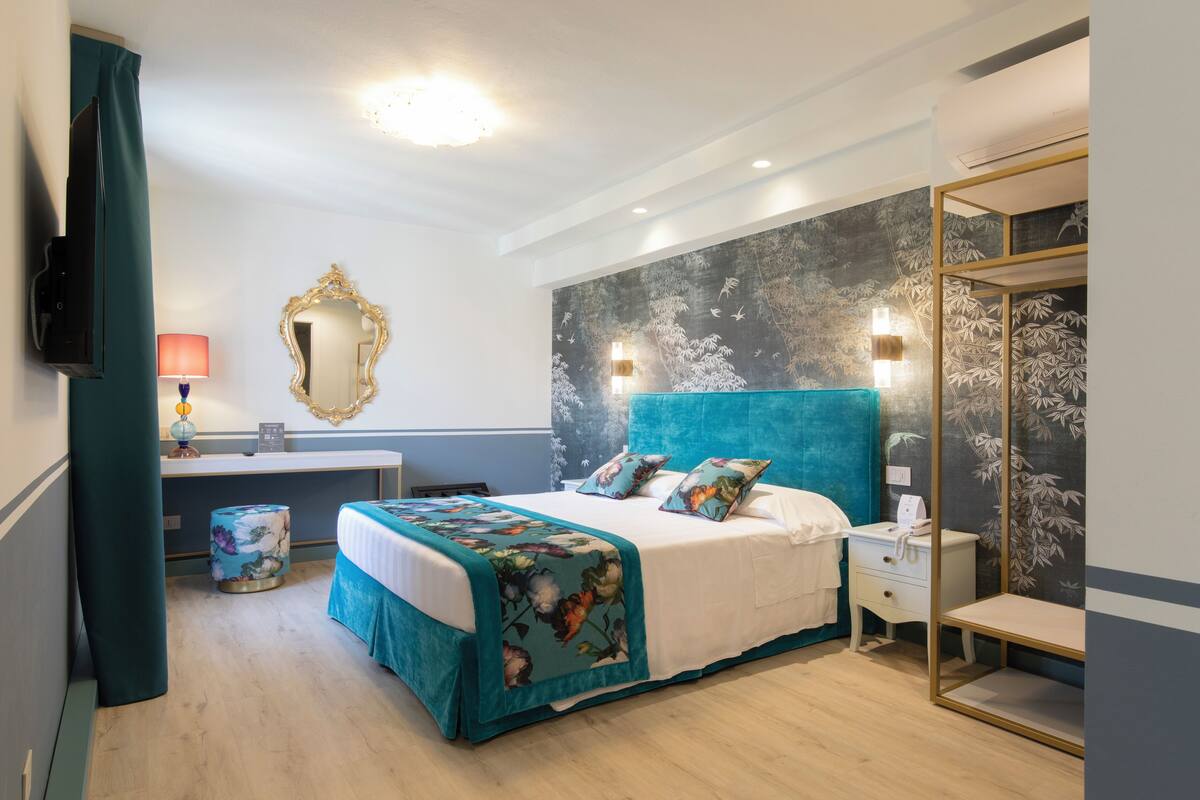 Une chambre moderne avec un grand lit, une table de chevet, un miroir et un mur orné d’une fresque sur le thème de la nature.