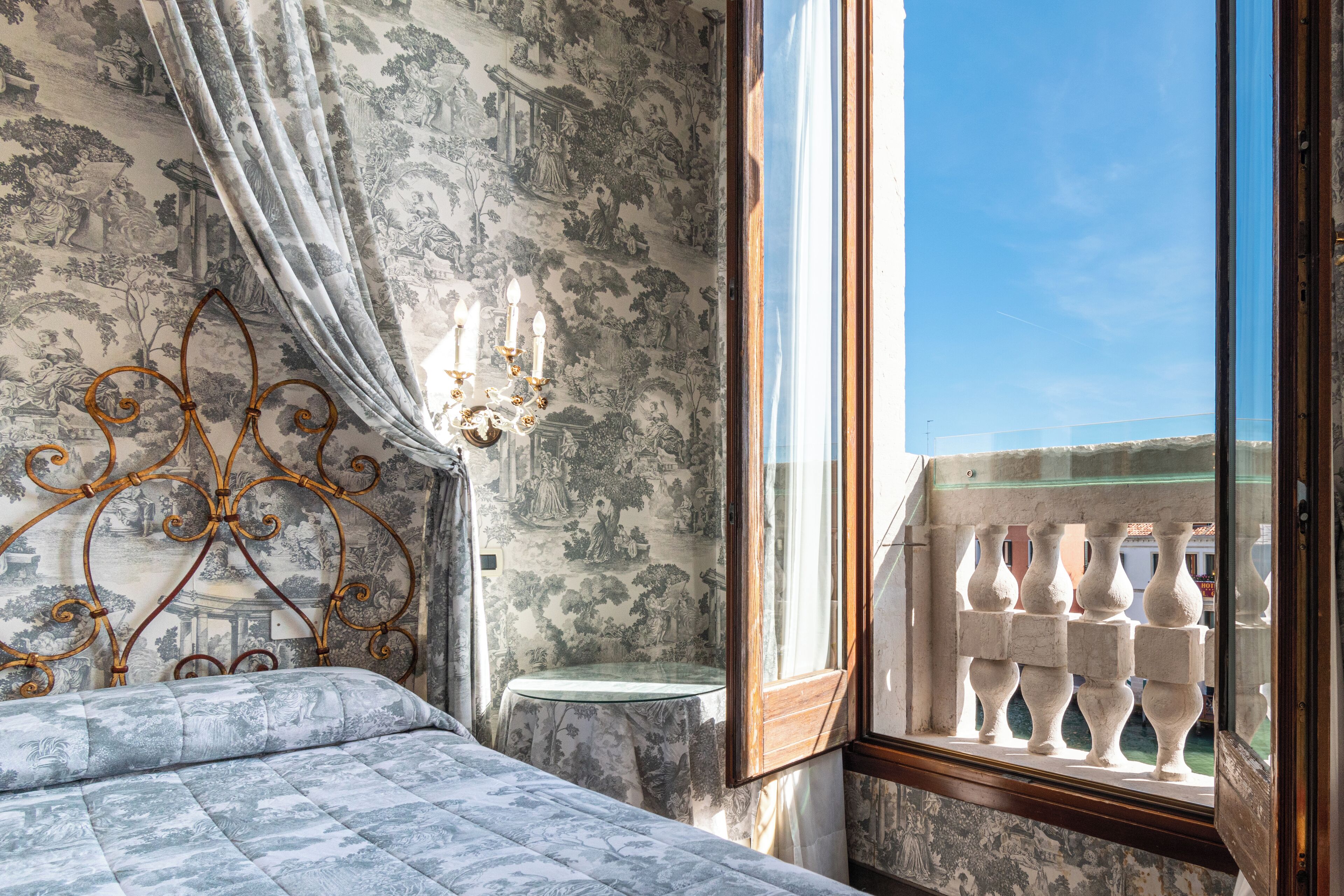 Una habitación con cama, una mesa y una ventana con vista a un balcón.