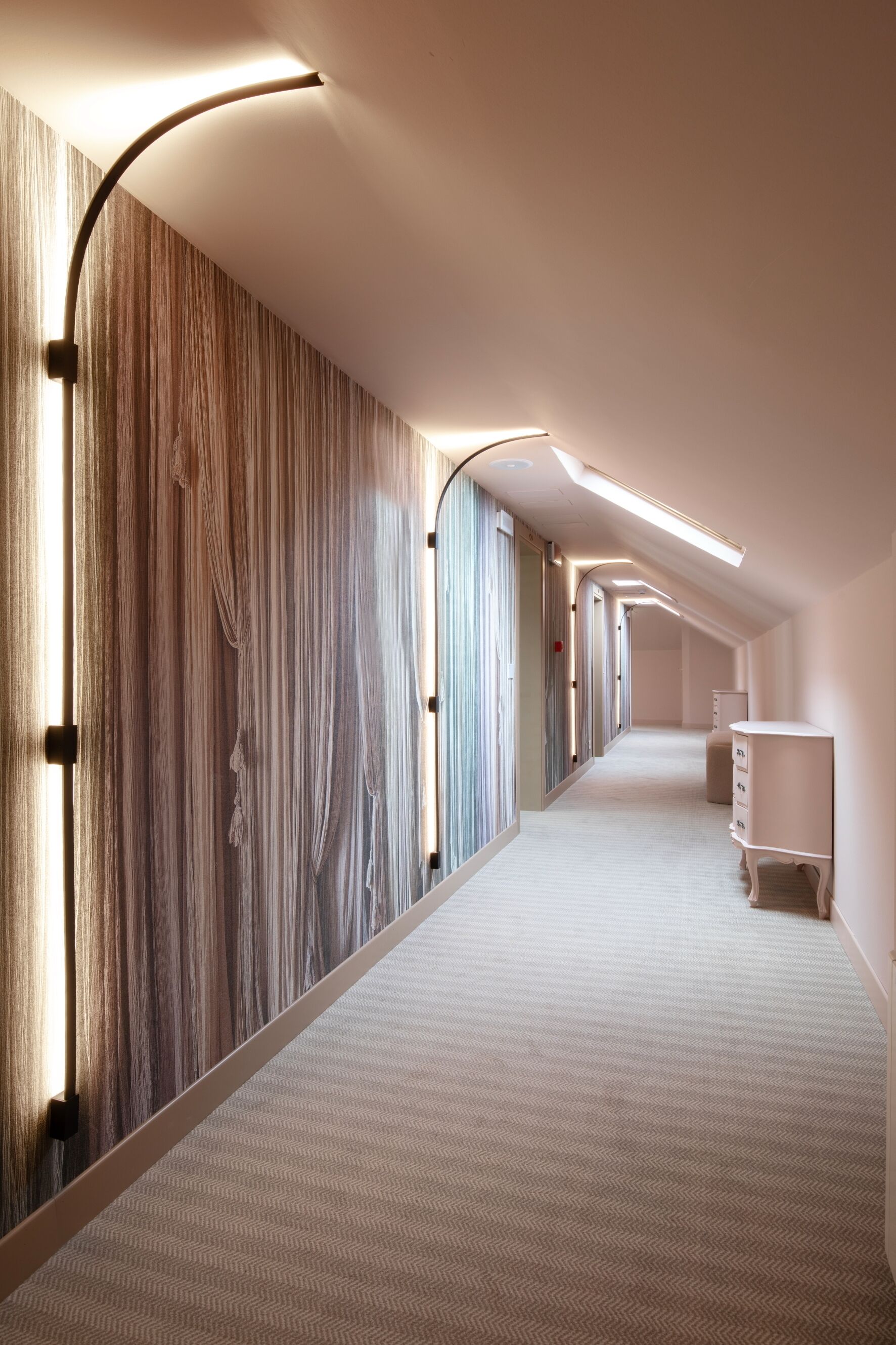 Un long couloir étroit, avec un mur orné de motifs sur un côté et un mur blanc de l’autre. Deux armoires blanches sont disposées le long du mur de droite.