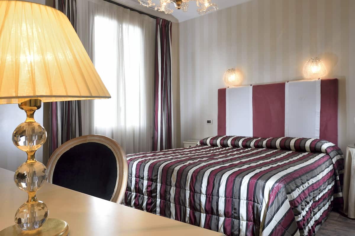 A hotel room with a bed, a desk, a lamp, and a chandelier.