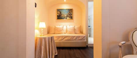 Una habitación de hotel con sofá, una mesa con lámpara, un cuadro en la pared y una silla.