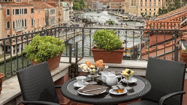 Un balcón con dos sillas de mimbre, una mesa dispuesta para el desayuno y vistas al Gran Canal de Venecia.