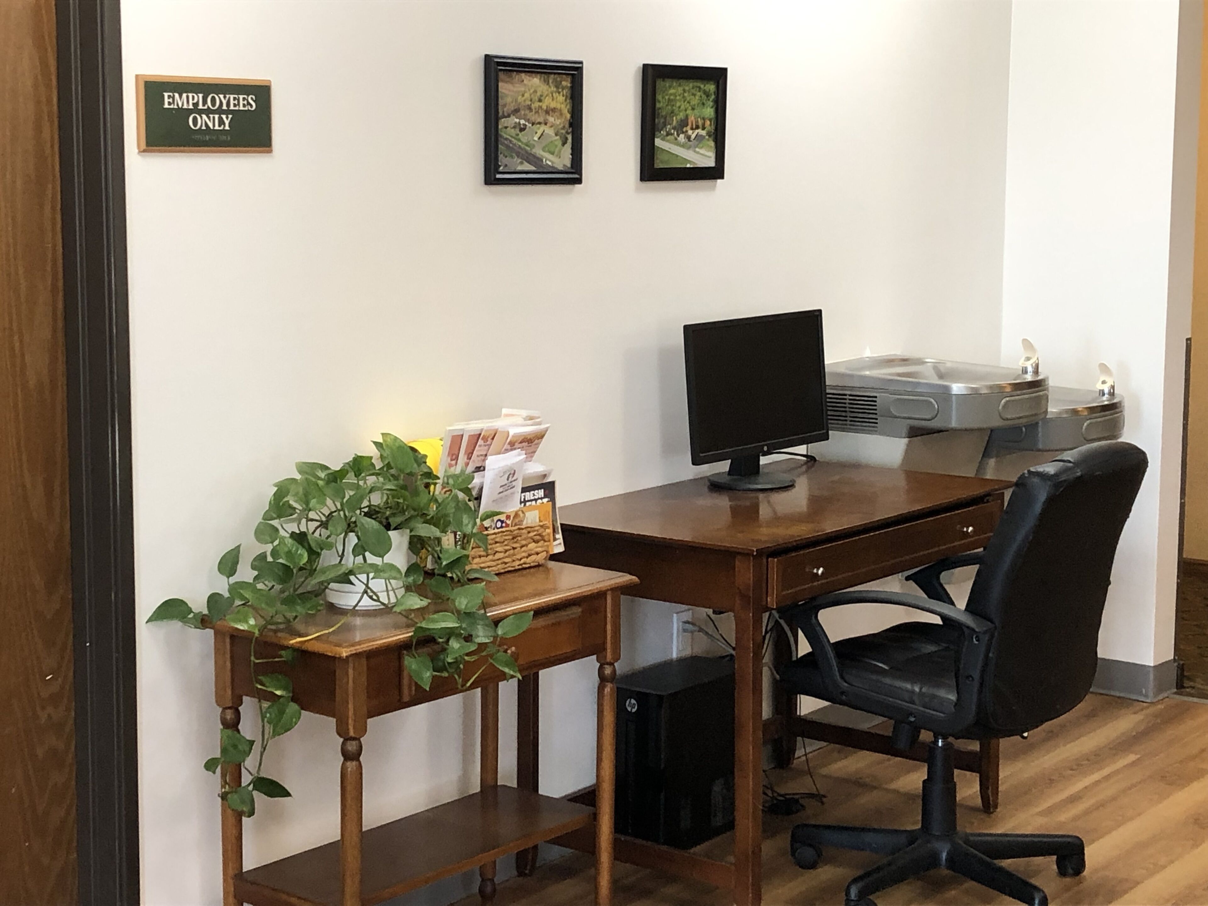 Un ufficio con scrivania, computer, sedia e due quadri appesi al muro.