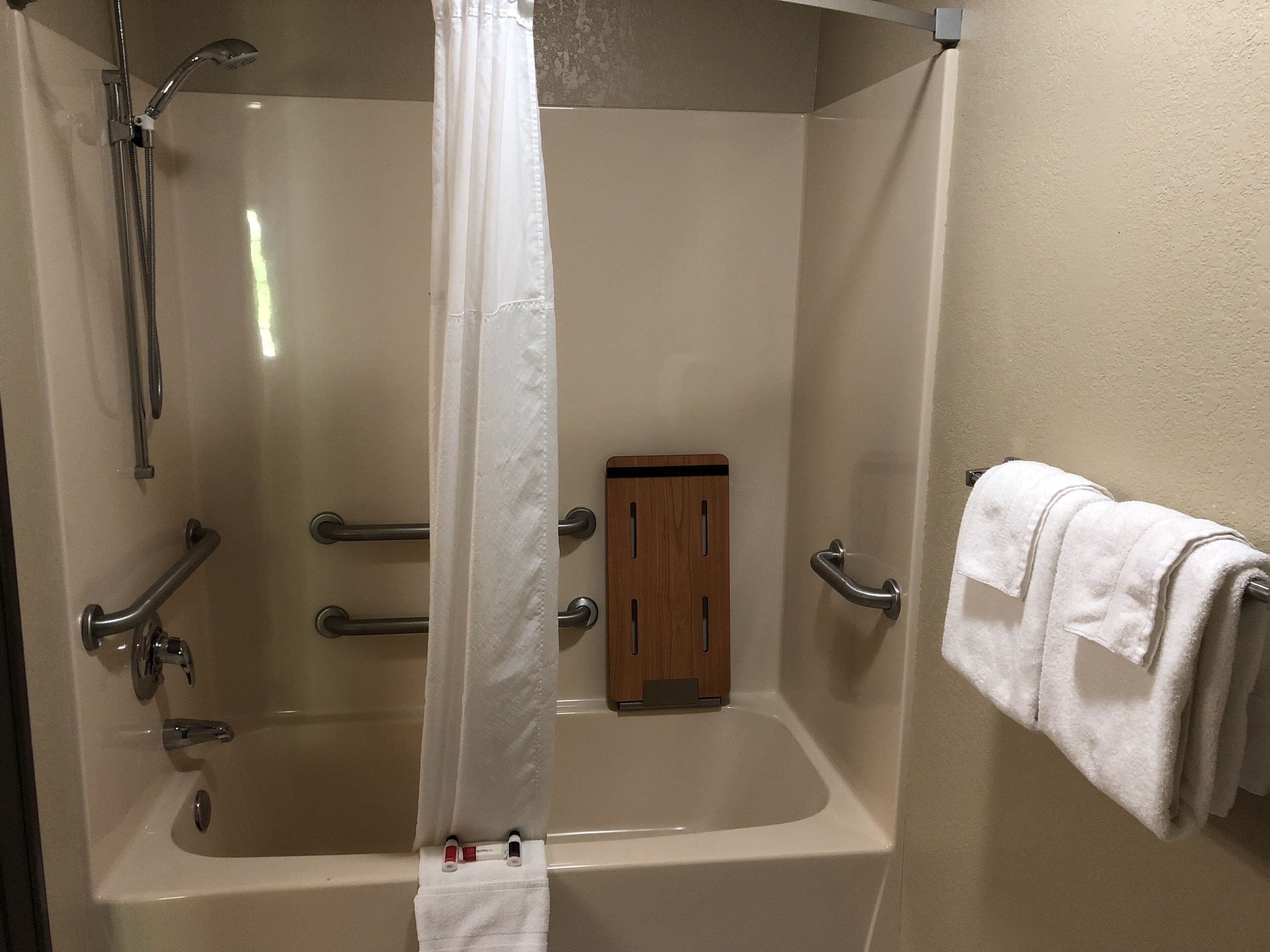 Un baño con bañera, ducha, barras de apoyo, un mueble de madera y un perchero para toallas.