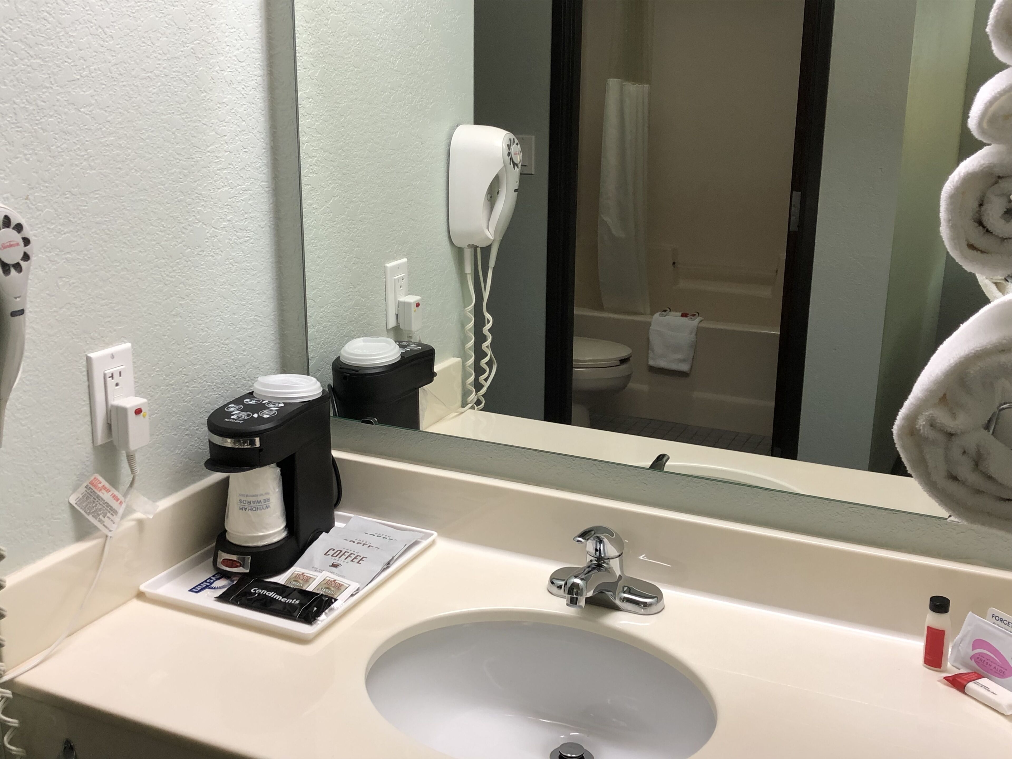 A hotel bathroom with a sink, a coffee maker, a hairdryer, and a towel.