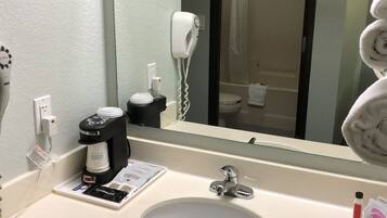 A hotel bathroom with a sink, a coffee maker, a hairdryer, and a towel.