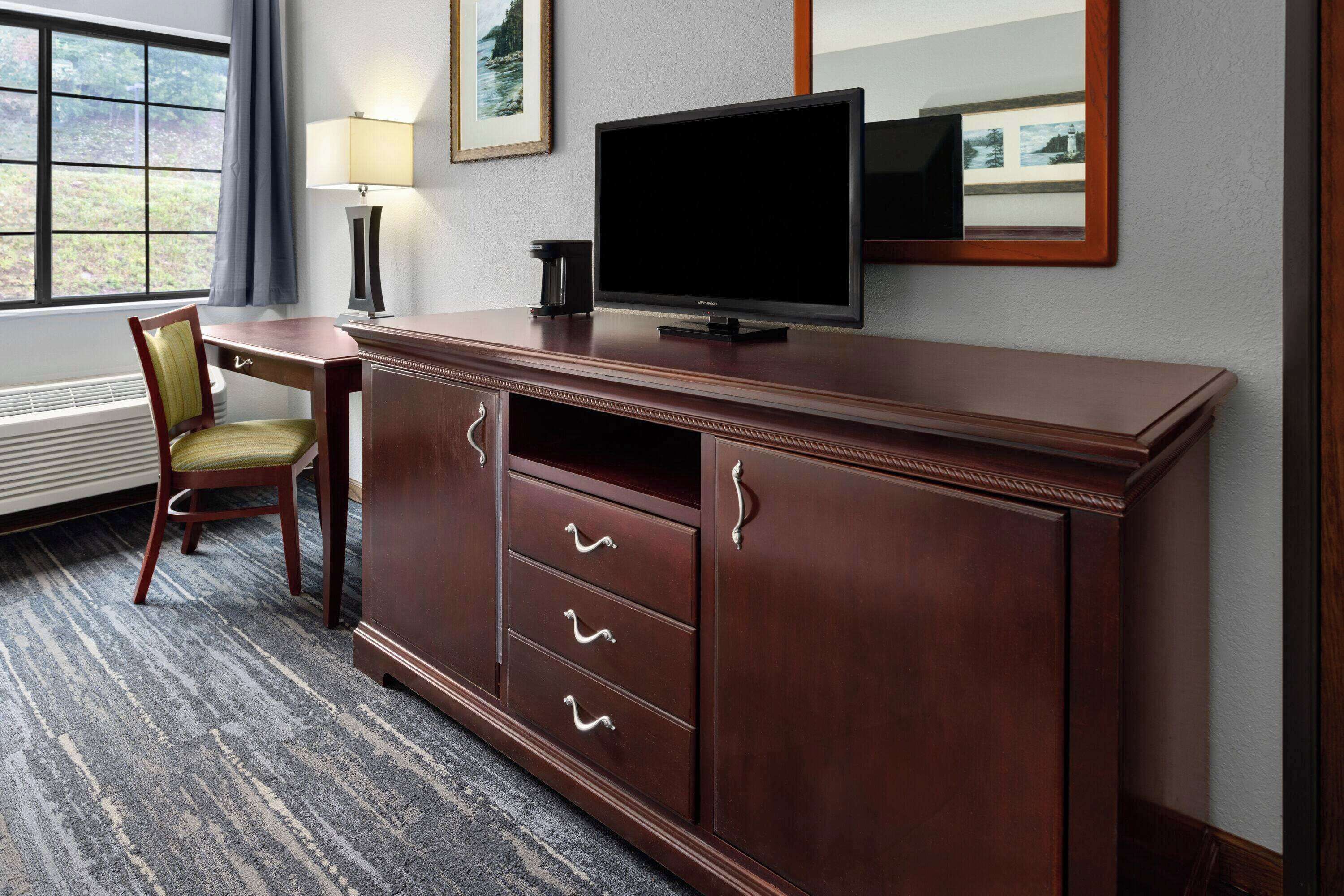 Habitación de hotel con un escritorio de madera, televisor, silla y ventana con vistas al exterior.