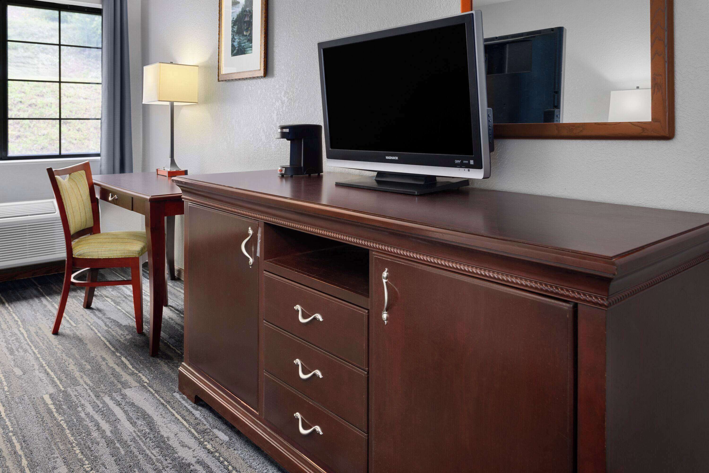 A hotel room with a wooden desk, a television, a lamp, and a chair.
