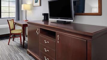 A hotel room with a wooden desk, a television, a lamp, and a chair.