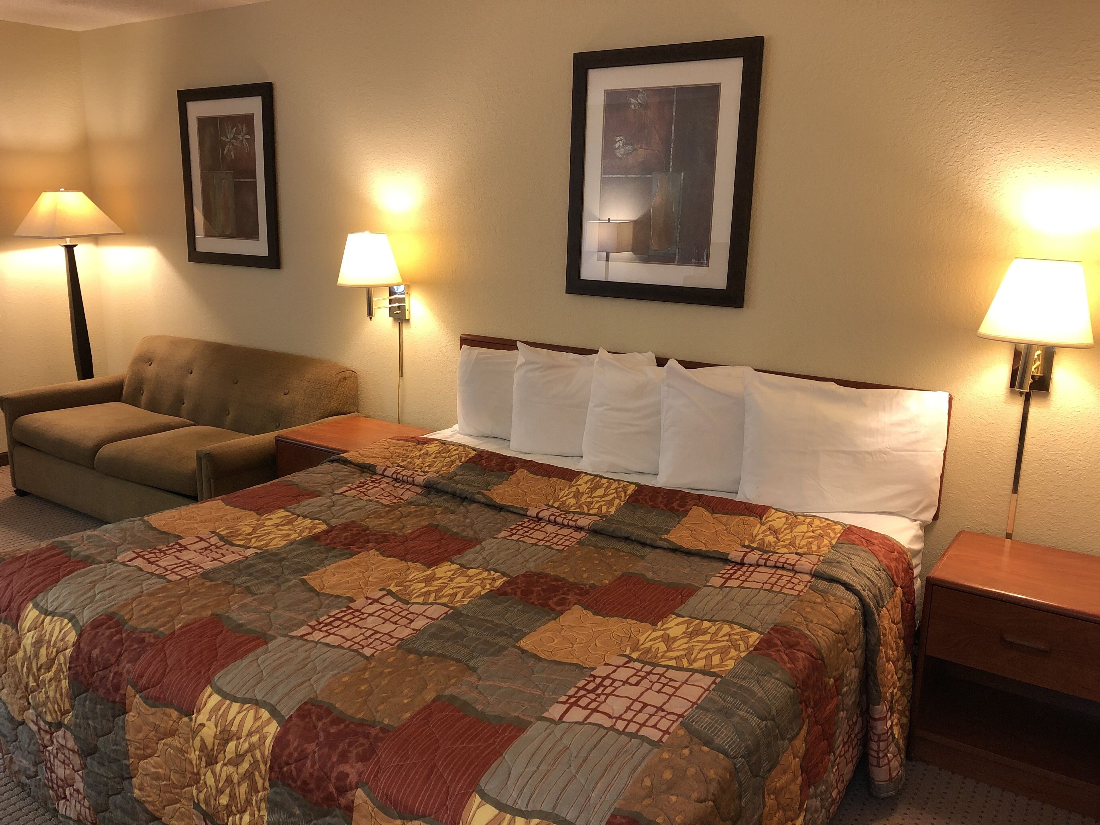 A hotel room with a large bed, a chair, two wall-mounted lamps, and two framed pictures on the wall.