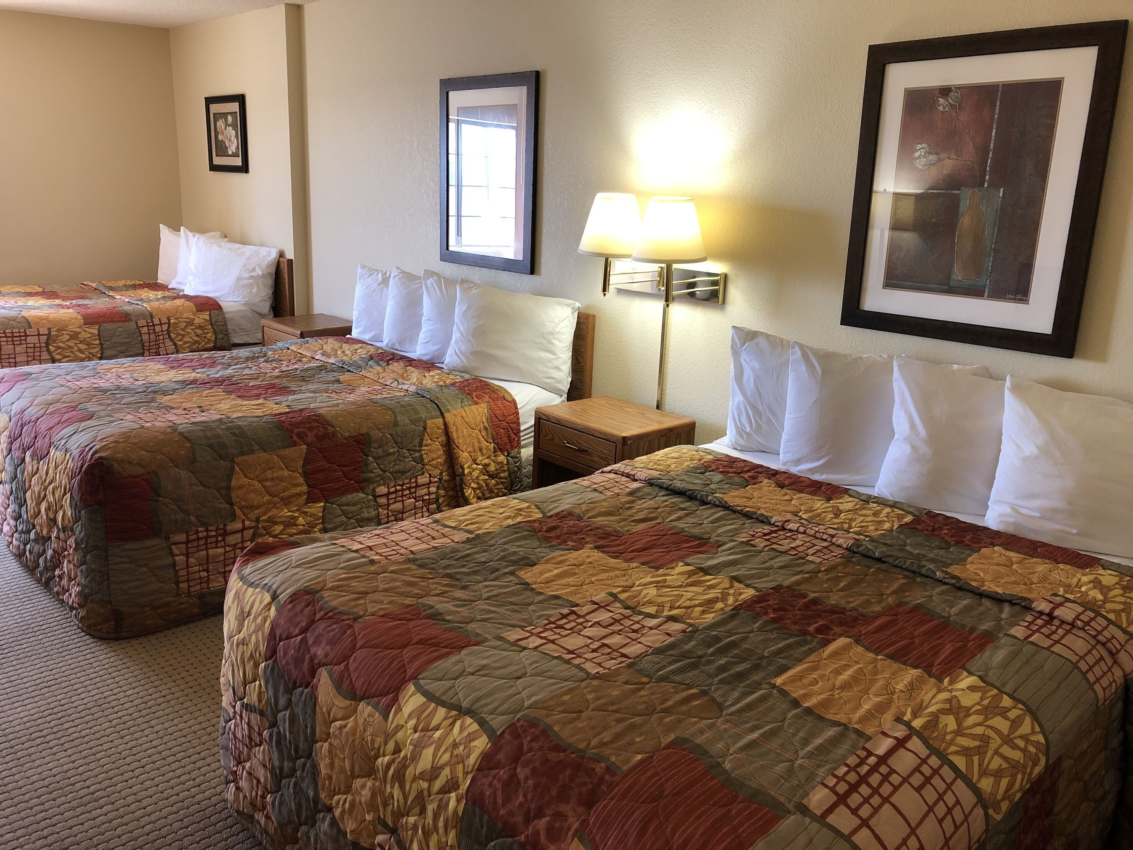 A hotel room with two beds, each with a quilted bedspread, a nightstand, a lamp, and framed artwork on the walls.