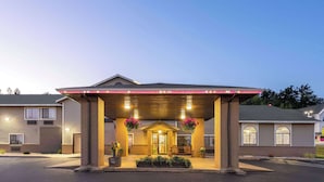 A motel with a covered entrance, a small porch with seating, and hanging flower baskets. - Days Inn by Wyndham Iron Mountain (Iron Mountain)