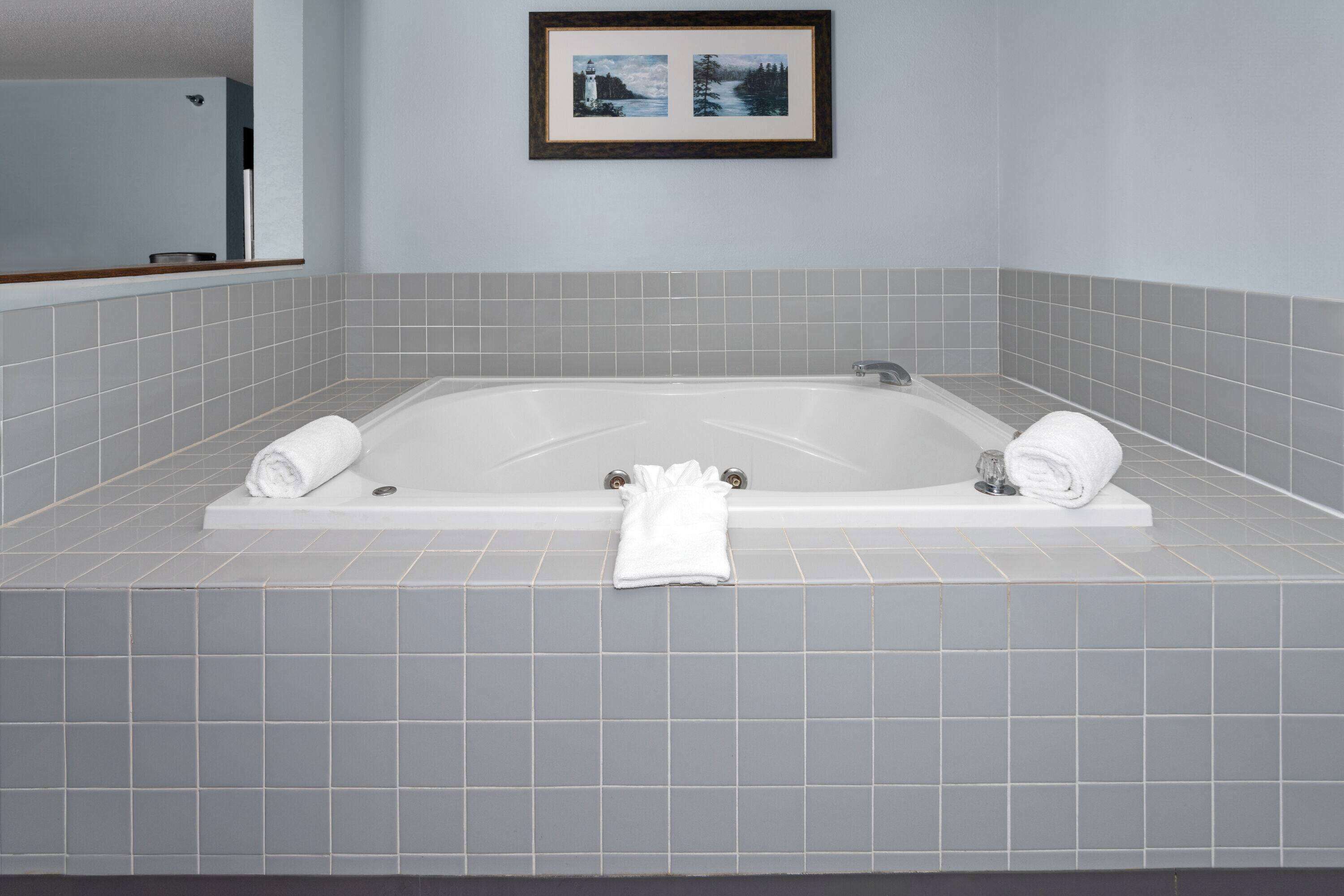Une salle de bain moderne avec une grande baignoire, des carreaux gris et un tableau encadré au mur.