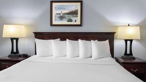 A neatly made bed with white bedding and a headboard, flanked by two bedside tables with lamps, and a framed picture above the bed. - Days Inn by Wyndham Iron Mountain (Iron Mountain)